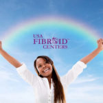Young Woman smiling, arms outstretched to the sky--a rainbow & the USA Fibroid Centers' logo above.