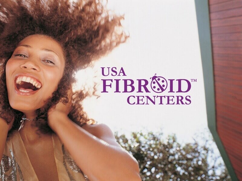 Happy woman, with hands on her neck and wide smile. USA Fibroid Centers Logo floats in the middle.