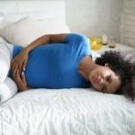 Woman laying on a bed experiencing abdominal pain from Uterine Fibroids