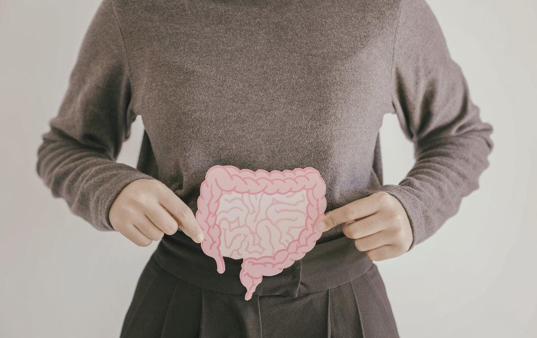 Constipation After Your Period: Understanding The Causes 3 A woman holding a paper cutout of intestines over her abdomen, illustrating digestive issues like constipation after a period.