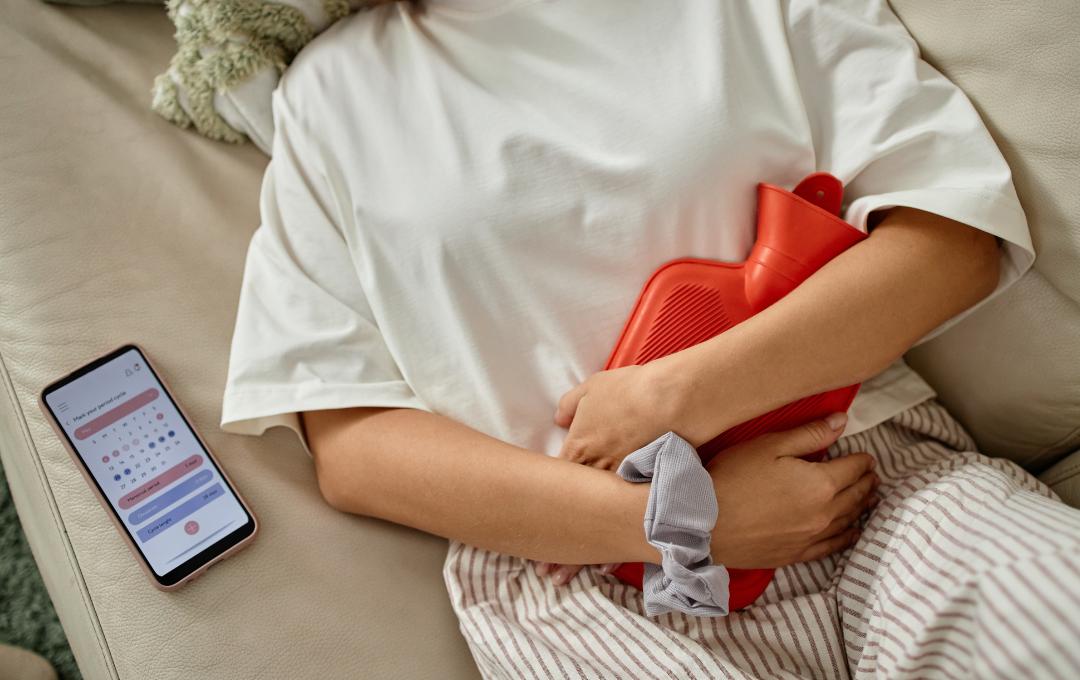 Can Fibroids Cause Headaches? 3 Woman experiencing severe cramp using hot water bottle for pain relief.
